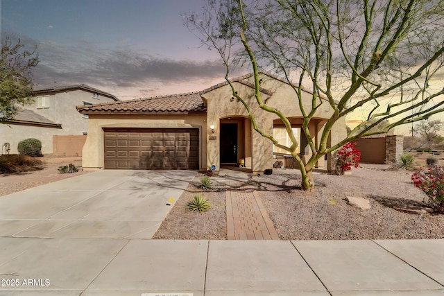 mediterranean / spanish-style house with driveway, a tiled roof, an attached garage, and stucco siding