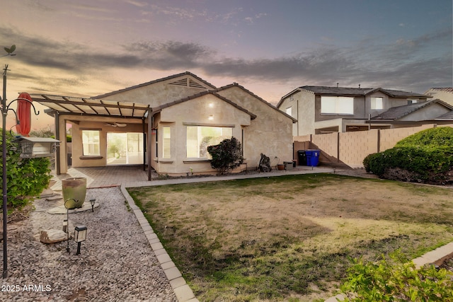 back of property at dusk with a patio area, stucco siding, fence, and a pergola