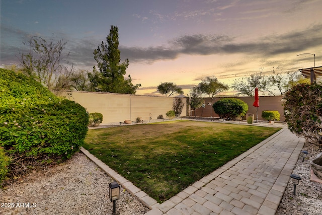 yard at dusk featuring a fenced backyard