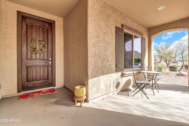 doorway to property featuring covered porch and stucco siding