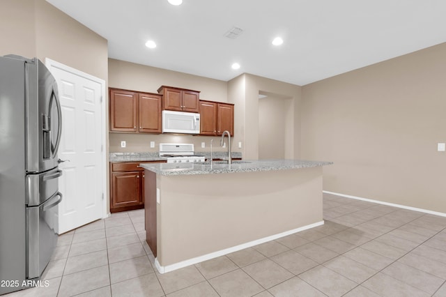 kitchen featuring white appliances, light tile patterned floors, an island with sink, light stone counters, and a sink