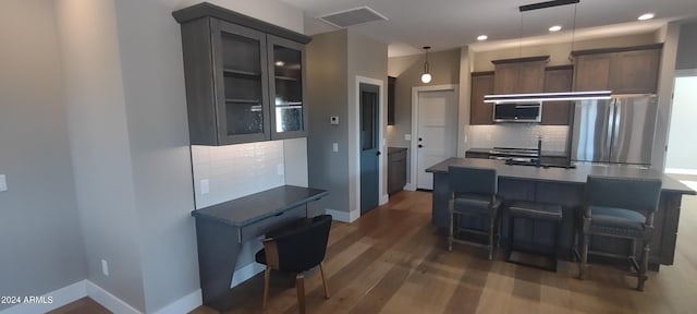 kitchen featuring stainless steel appliances, dark wood-type flooring, hanging light fixtures, tasteful backsplash, and a kitchen breakfast bar