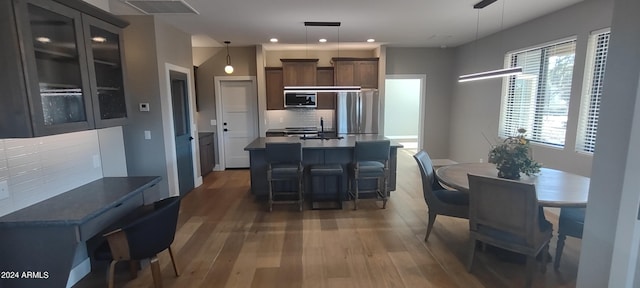 kitchen with a kitchen breakfast bar, hanging light fixtures, tasteful backsplash, dark brown cabinets, and dark hardwood / wood-style flooring