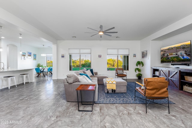 living area with baseboards, arched walkways, and a ceiling fan