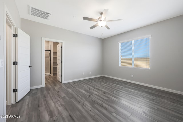 unfurnished bedroom with a walk in closet, dark hardwood / wood-style floors, and ceiling fan