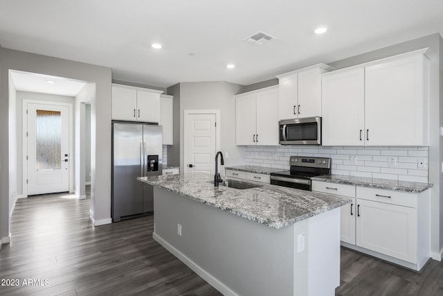 kitchen featuring white cabinets, stainless steel appliances, light stone countertops, and an island with sink