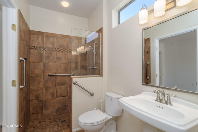 bathroom with toilet, a tile shower, and sink