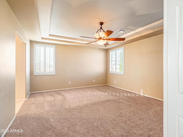 empty room with light colored carpet, ceiling fan, and a tray ceiling