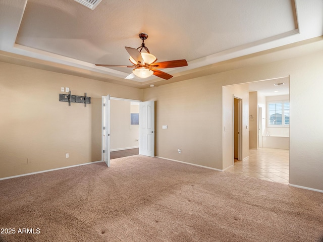 unfurnished room with a raised ceiling, ceiling fan, and light carpet