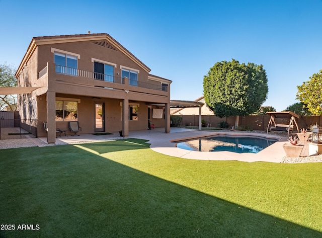 rear view of house with a balcony, a patio, a fenced in pool, and a lawn