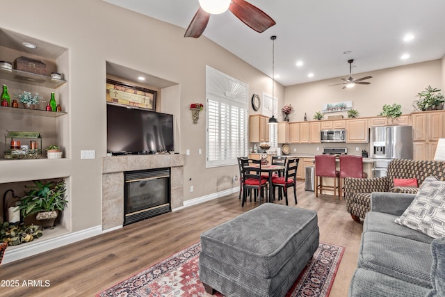 living room with built in shelves, ceiling fan, light hardwood / wood-style flooring, and a tile fireplace