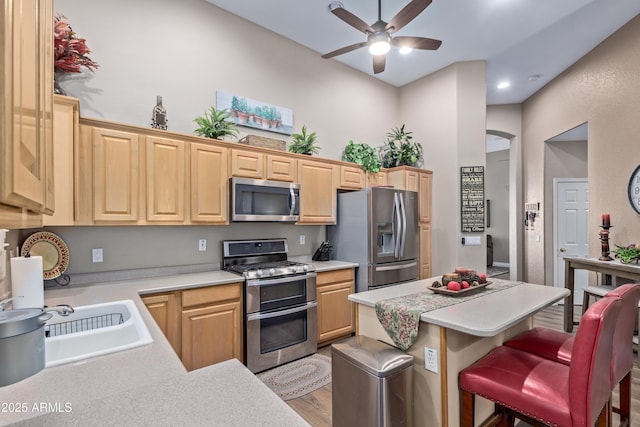 kitchen featuring ceiling fan, light brown cabinets, stainless steel appliances, a kitchen breakfast bar, and light hardwood / wood-style floors