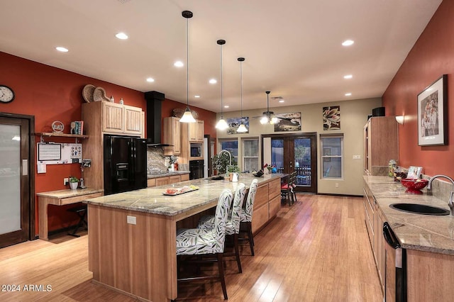 kitchen with light wood-type flooring, a large island with sink, black appliances, and sink