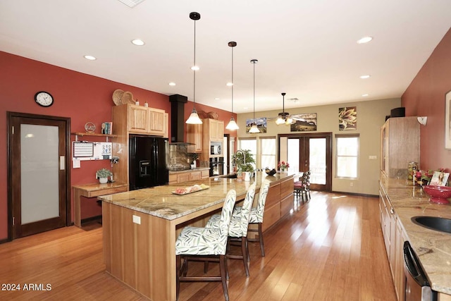 kitchen featuring light stone countertops, a center island with sink, black appliances, and french doors