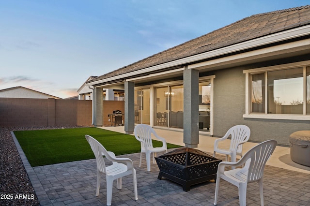 patio terrace at dusk featuring an outdoor fire pit, a yard, and a grill