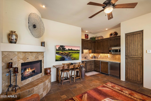 7731 E Soaring Eagle Way, Scottsdale, AZ 85266 - kitchen featuring stainless steel microwave, stone tile floors, light countertops, dark brown cabinets, and a fireplace