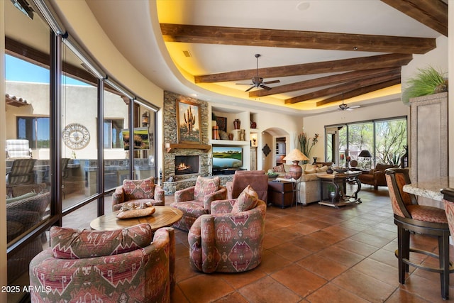 7731 E Soaring Eagle Way, Scottsdale, AZ 85266 - living area featuring ceiling fan, arched walkways, dark tile patterned floors, a stone fireplace, and beamed ceiling
