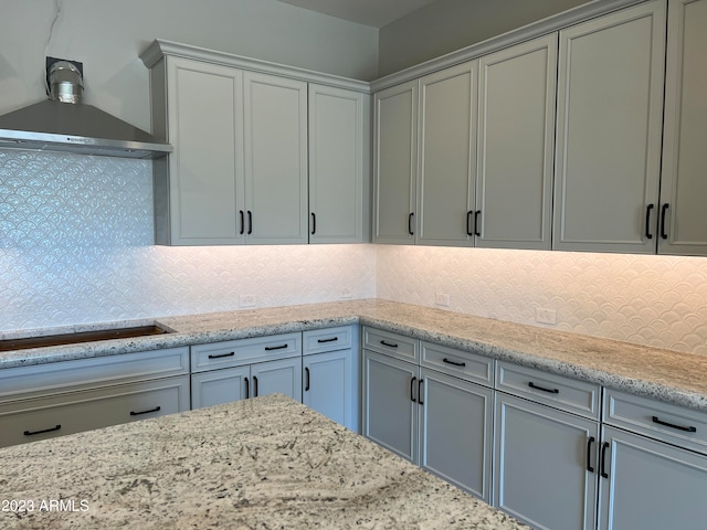 kitchen featuring backsplash, light stone countertops, wall chimney range hood, and stovetop