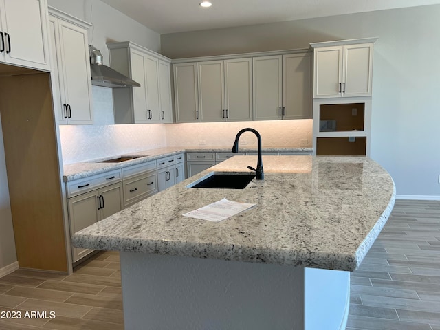 kitchen featuring wall chimney exhaust hood, black electric stovetop, white cabinetry, sink, and light stone counters