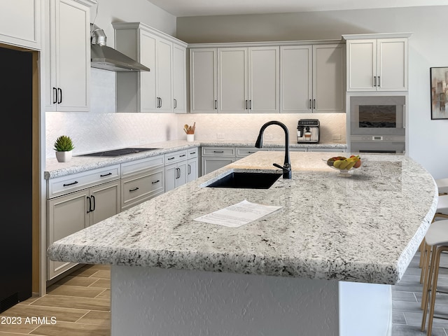 kitchen with light stone countertops, backsplash, wall chimney exhaust hood, sink, and a breakfast bar