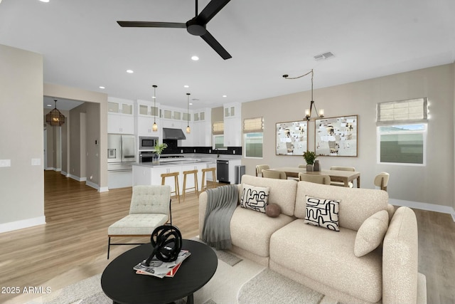 living room featuring recessed lighting, baseboards, light wood-style flooring, and ceiling fan with notable chandelier