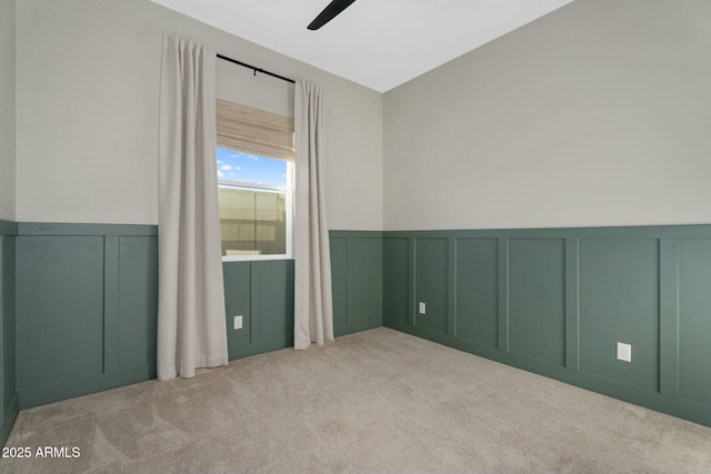 empty room featuring carpet floors, ceiling fan, wainscoting, and a decorative wall