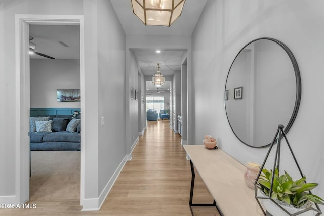 hall featuring visible vents, light wood-style flooring, and baseboards