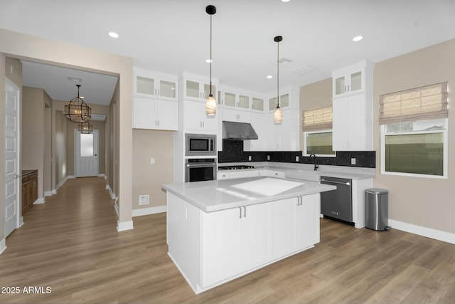 kitchen with under cabinet range hood, a sink, a center island, stainless steel appliances, and decorative backsplash