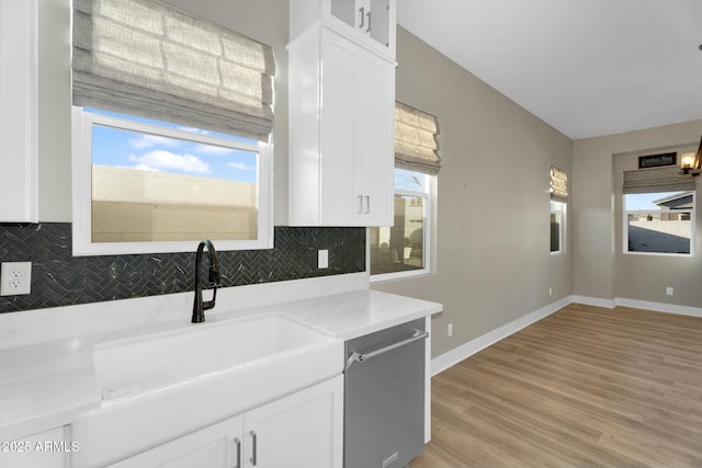 kitchen with stainless steel dishwasher, white cabinetry, backsplash, and a sink
