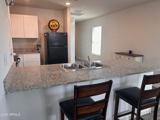 kitchen with freestanding refrigerator, white cabinetry, a sink, and a kitchen bar