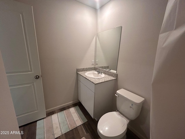 half bath featuring toilet, baseboards, wood finished floors, and vanity