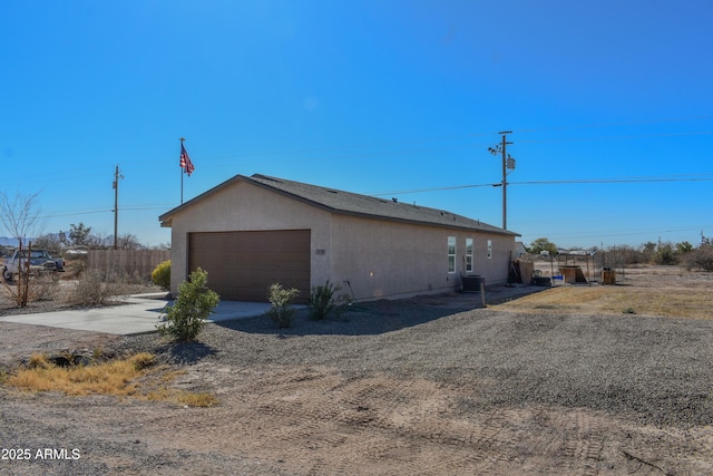 view of home's exterior featuring a garage, concrete driveway, fence, central air condition unit, and stucco siding