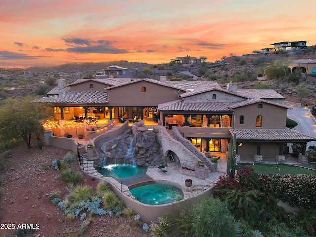 back house at dusk with an in ground hot tub and a patio area