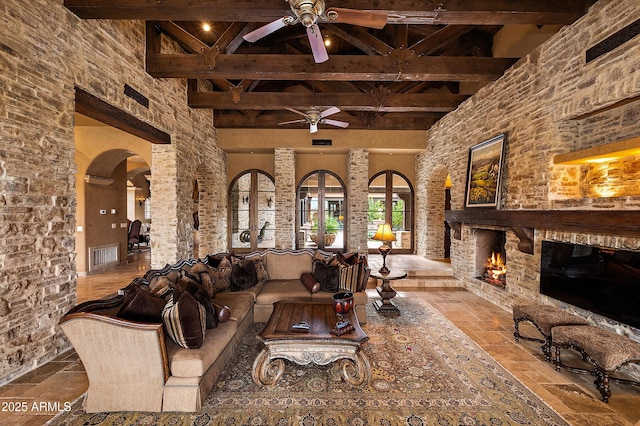 unfurnished living room with a high ceiling, french doors, ceiling fan, an outdoor stone fireplace, and beam ceiling