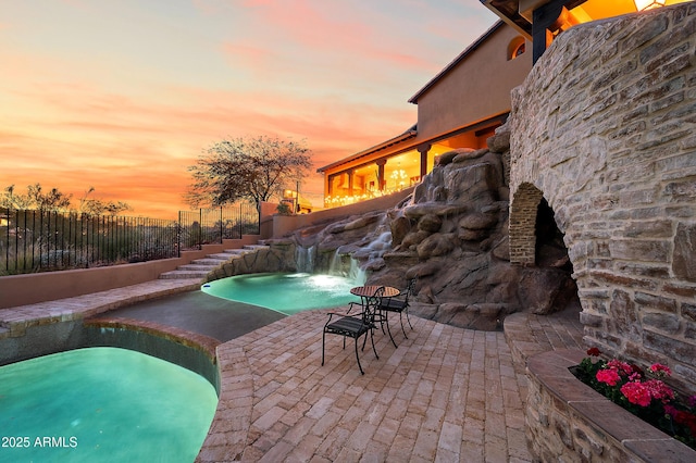 pool at dusk featuring pool water feature, a patio, a jacuzzi, and an outdoor fireplace