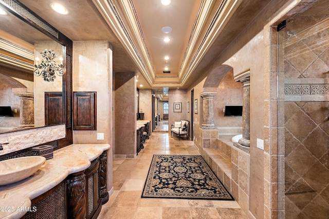 bathroom with a tub to relax in, ornate columns, vanity, a raised ceiling, and crown molding