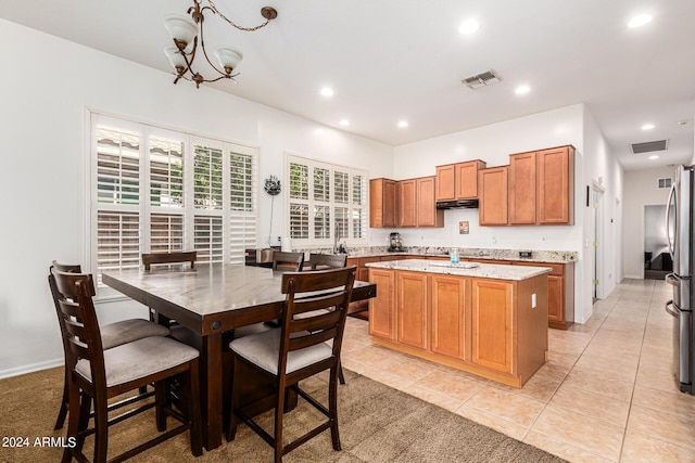 kitchen featuring pendant lighting, a center island, an inviting chandelier, light stone countertops, and light tile patterned flooring