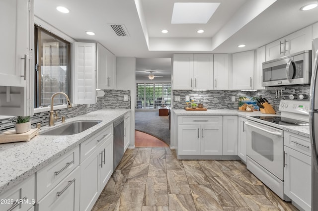 kitchen featuring sink, appliances with stainless steel finishes, white cabinetry, a skylight, and light stone countertops