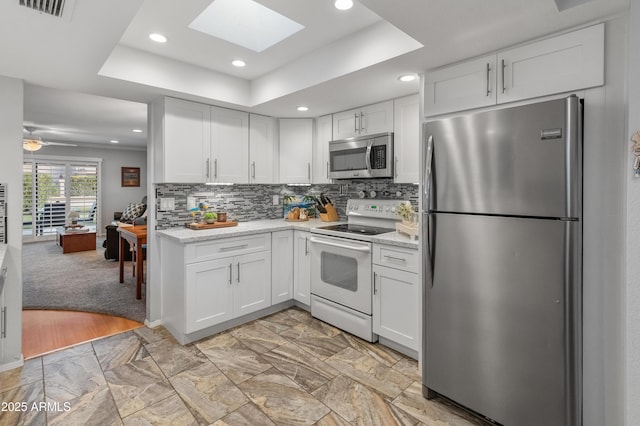 kitchen with appliances with stainless steel finishes, white cabinets, and a tray ceiling