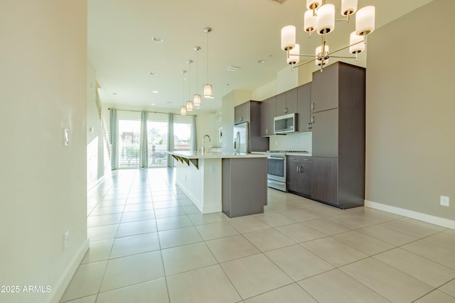 kitchen featuring appliances with stainless steel finishes, tasteful backsplash, hanging light fixtures, a kitchen island with sink, and a notable chandelier