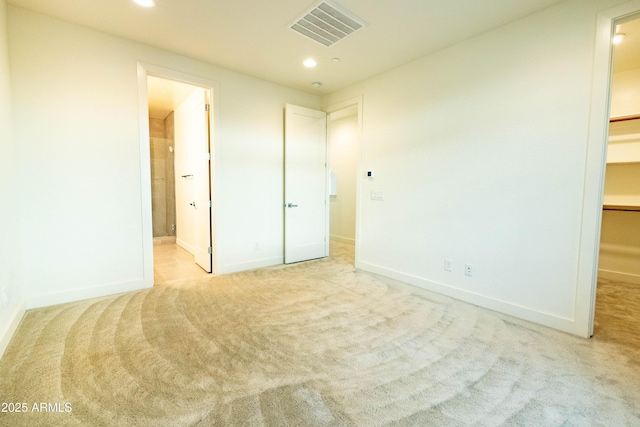 unfurnished bedroom featuring light carpet, a spacious closet, and ensuite bath