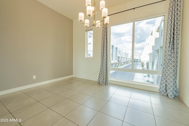 tiled spare room featuring plenty of natural light and an inviting chandelier