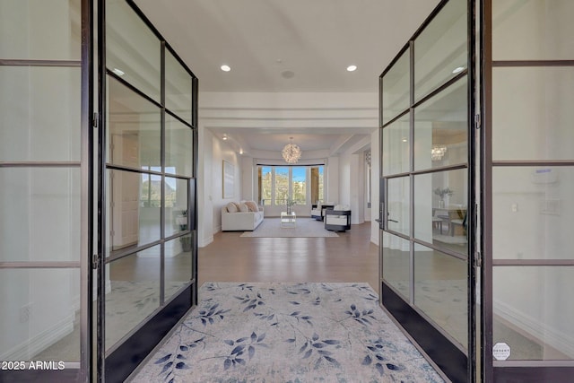 corridor with french doors, wood-type flooring, and an inviting chandelier