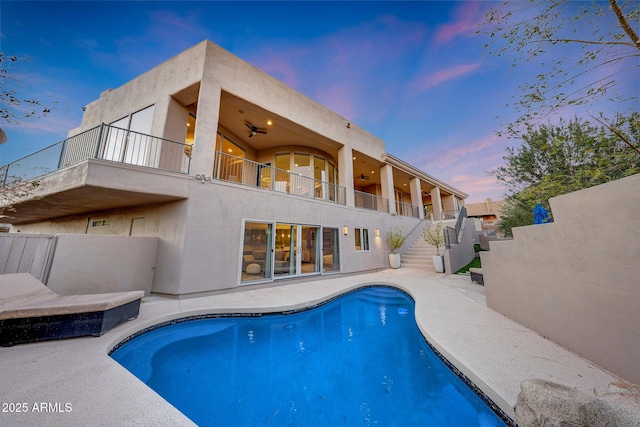 pool at dusk with a patio area and ceiling fan