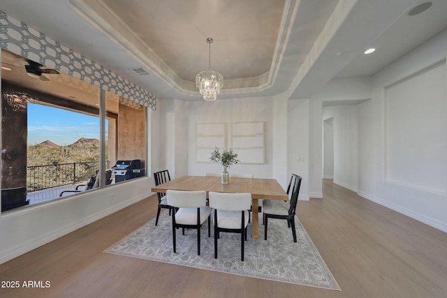 dining area with light hardwood / wood-style floors, a chandelier, a tray ceiling, and crown molding