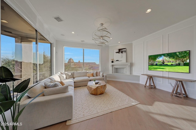 living room with an inviting chandelier, ornamental molding, and light hardwood / wood-style flooring