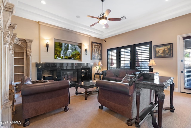 carpeted living room featuring ceiling fan, a wealth of natural light, a raised ceiling, and a high end fireplace