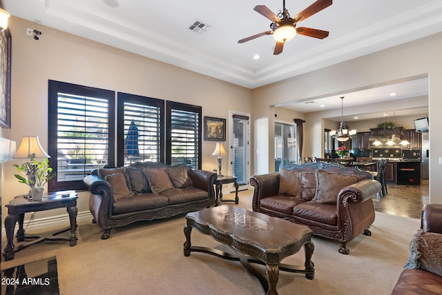 living room with ceiling fan with notable chandelier, a raised ceiling, and carpet floors