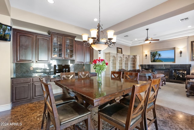 carpeted dining space featuring a raised ceiling, ceiling fan with notable chandelier, and a tile fireplace