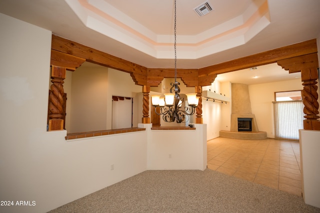 carpeted empty room featuring a notable chandelier, a raised ceiling, and a fireplace